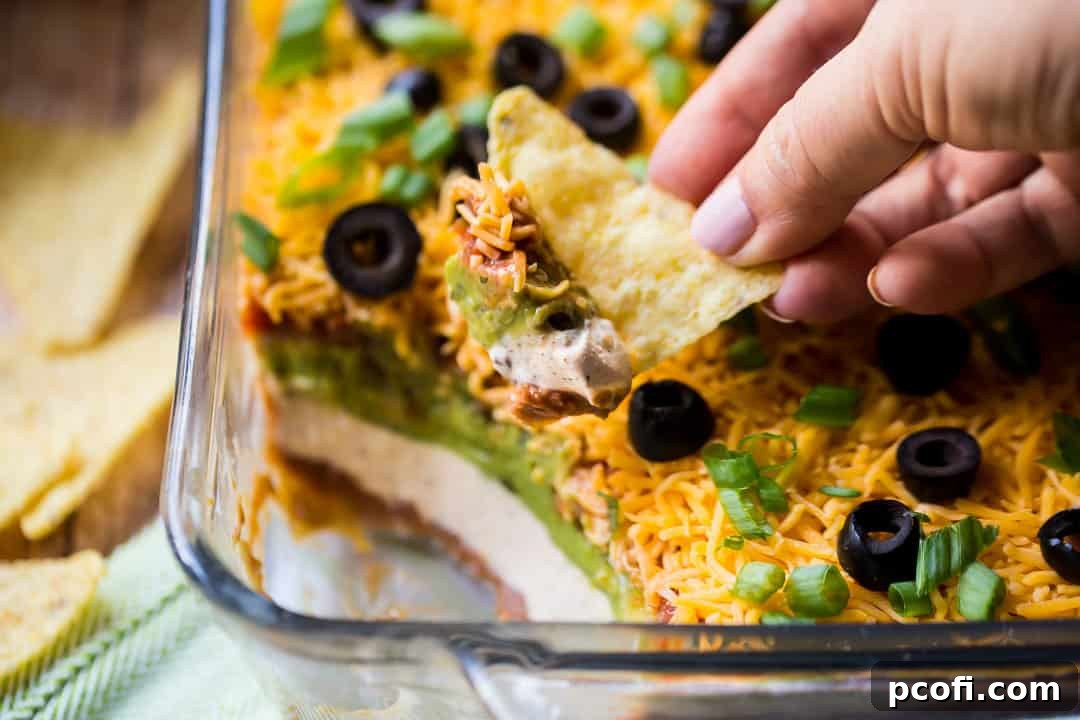 A corn chip perfectly poised, lifting a generous scoop of the colorful 7-Layer Dip, clearly displaying its distinct, vibrant layers of fresh ingredients and inviting texture.