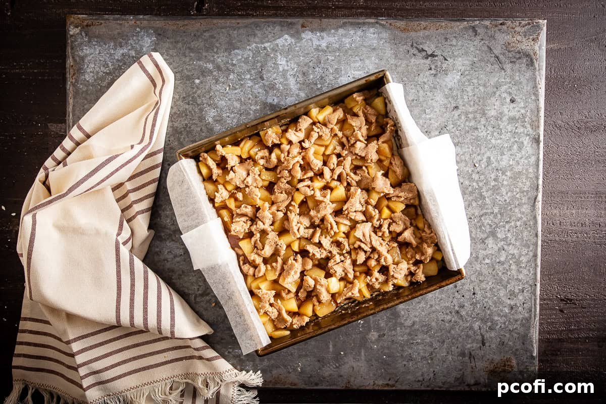 Freshly baked apple pie bars showcasing a golden-brown crumb topping and a rich apple filling, still in the square baking pan.