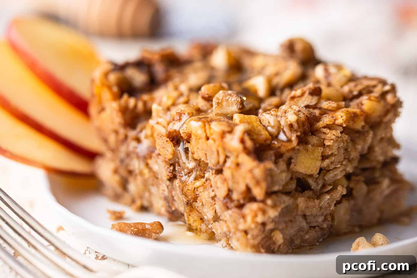 A close-up of a square of easy Baked Oatmeal, elegantly served with fresh sliced apples, a drizzle of honey, and crunchy walnuts.