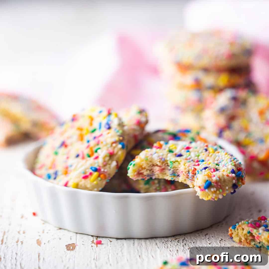 A vibrant collection of Funfetti cookies piled high in a small white ceramic dish, with more colorful cookies stacked nearby.