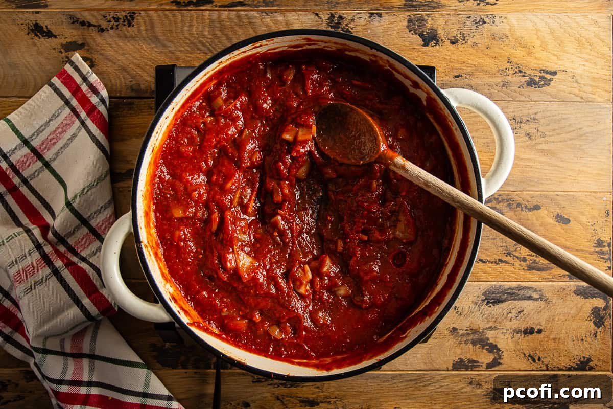 Rich red Braciole sauce being stirred in a Dutch oven with a wooden spoon.
