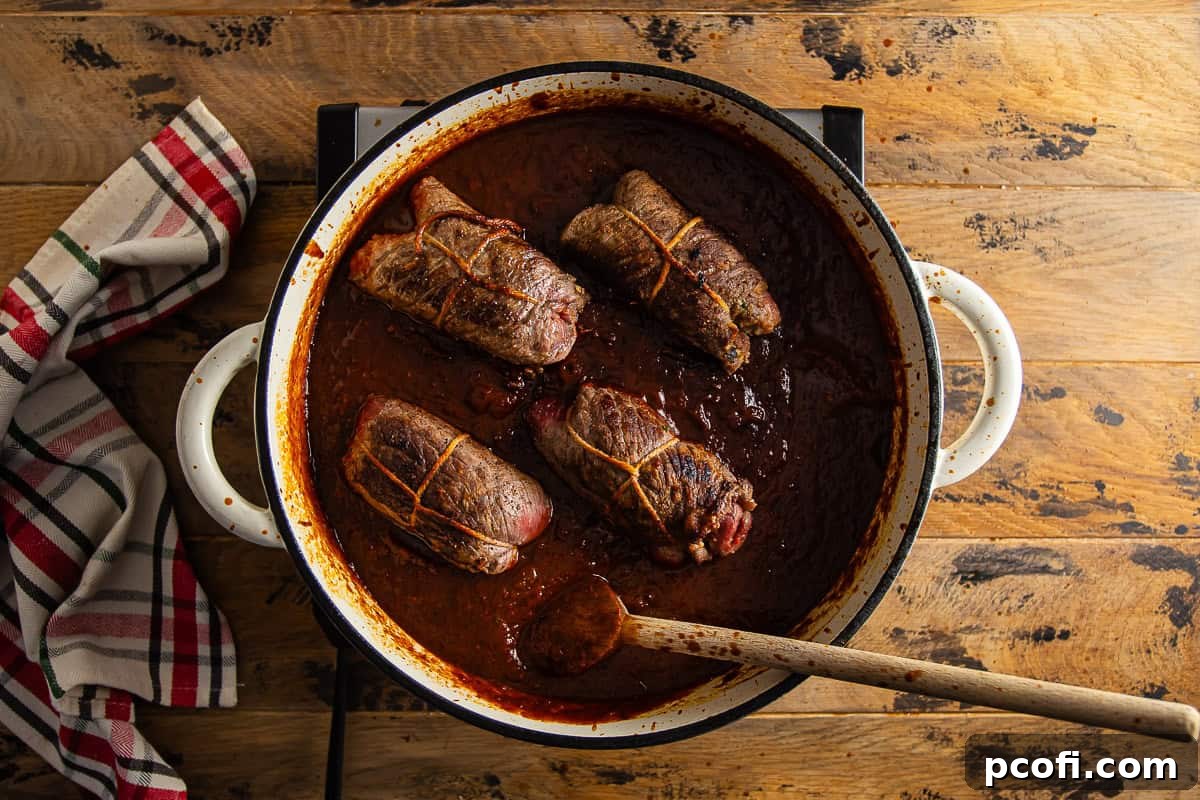 Seared Braciole beef rolls returned to a Dutch oven, submerged in the tomato sauce for braising.
