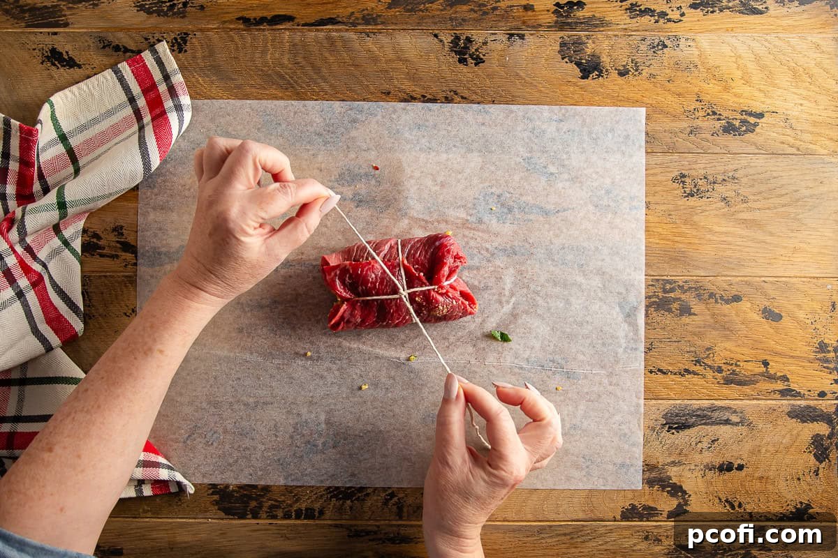 Braciole beef rolls being tied with kitchen string to secure the filling.