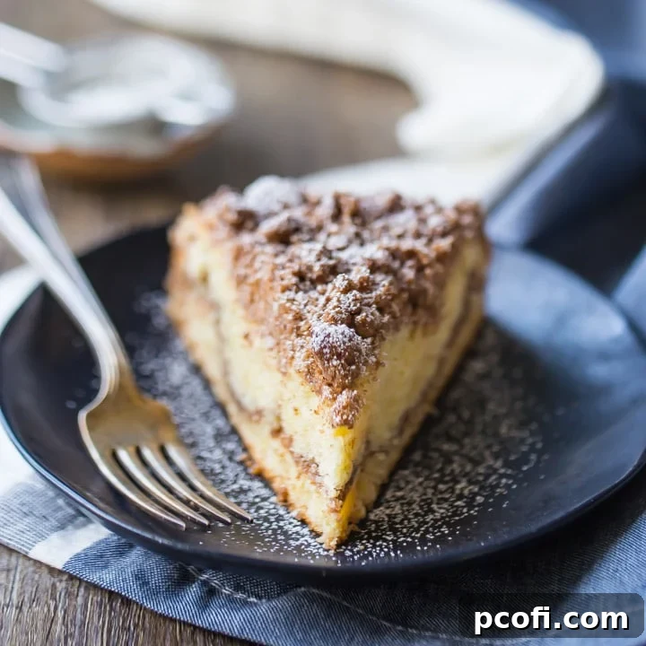 A thick slice of cinnamon crumb cake, elegantly displayed on a dark blue plate, dusted with powdered sugar, showcasing its moist texture and generous streusel topping.