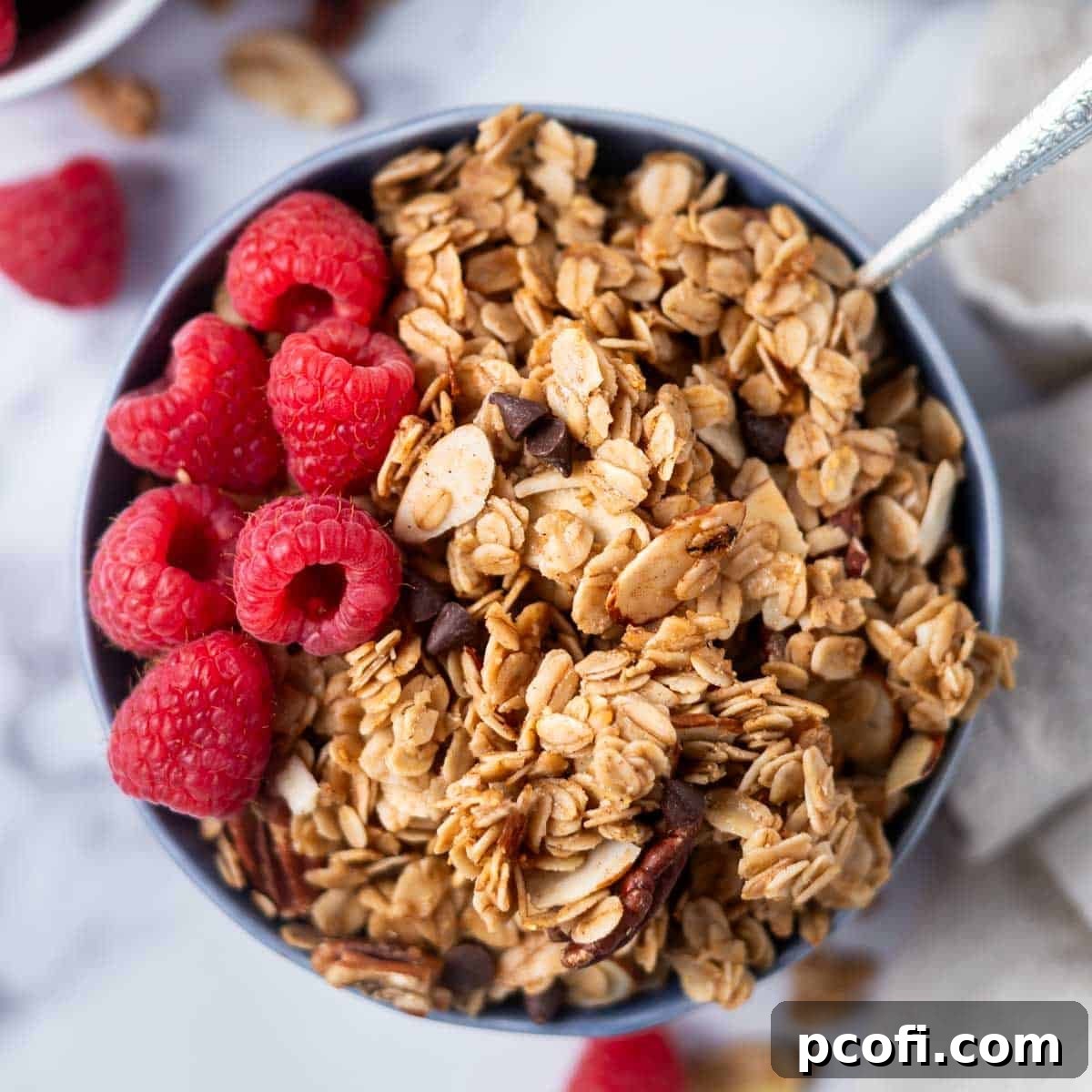 A bowl of homemade maple granola with brown sugar and pecans, ready to be served with a spoon.