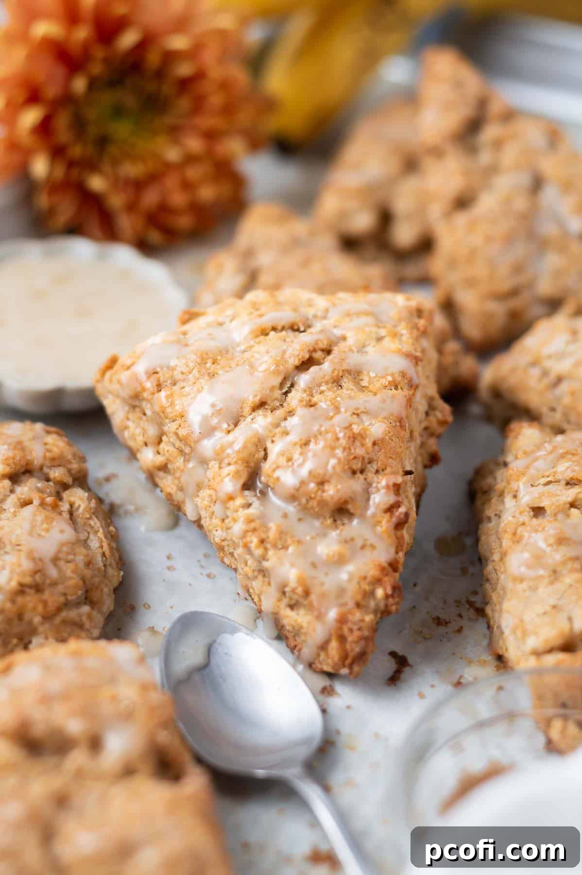 Freshly baked banana scones with a sweet banana glaze on a parchment-lined baking sheet, adorned with flowers and ripe bananas in the background.