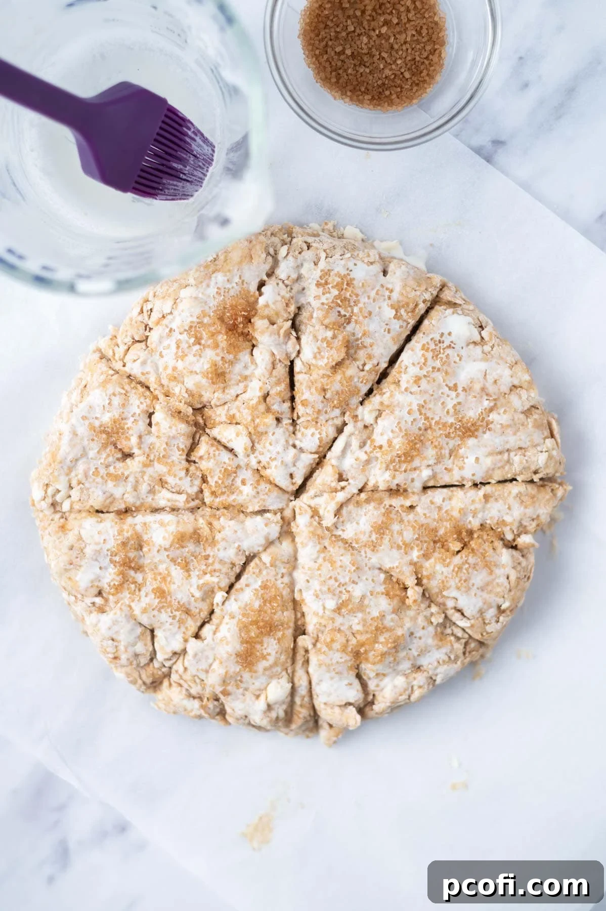 An overhead view of scone dough perfectly cut into eight equal triangles, brushed with heavy cream and sprinkled with turbinado sugar before baking.