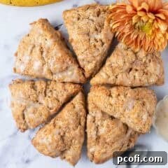 An overhead view of golden-brown banana scones resting on a cooling rack, with a vibrant orange flower nearby.