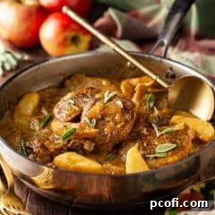 Pork chops with apples in a stainless steel skillet with whole apples in the background.