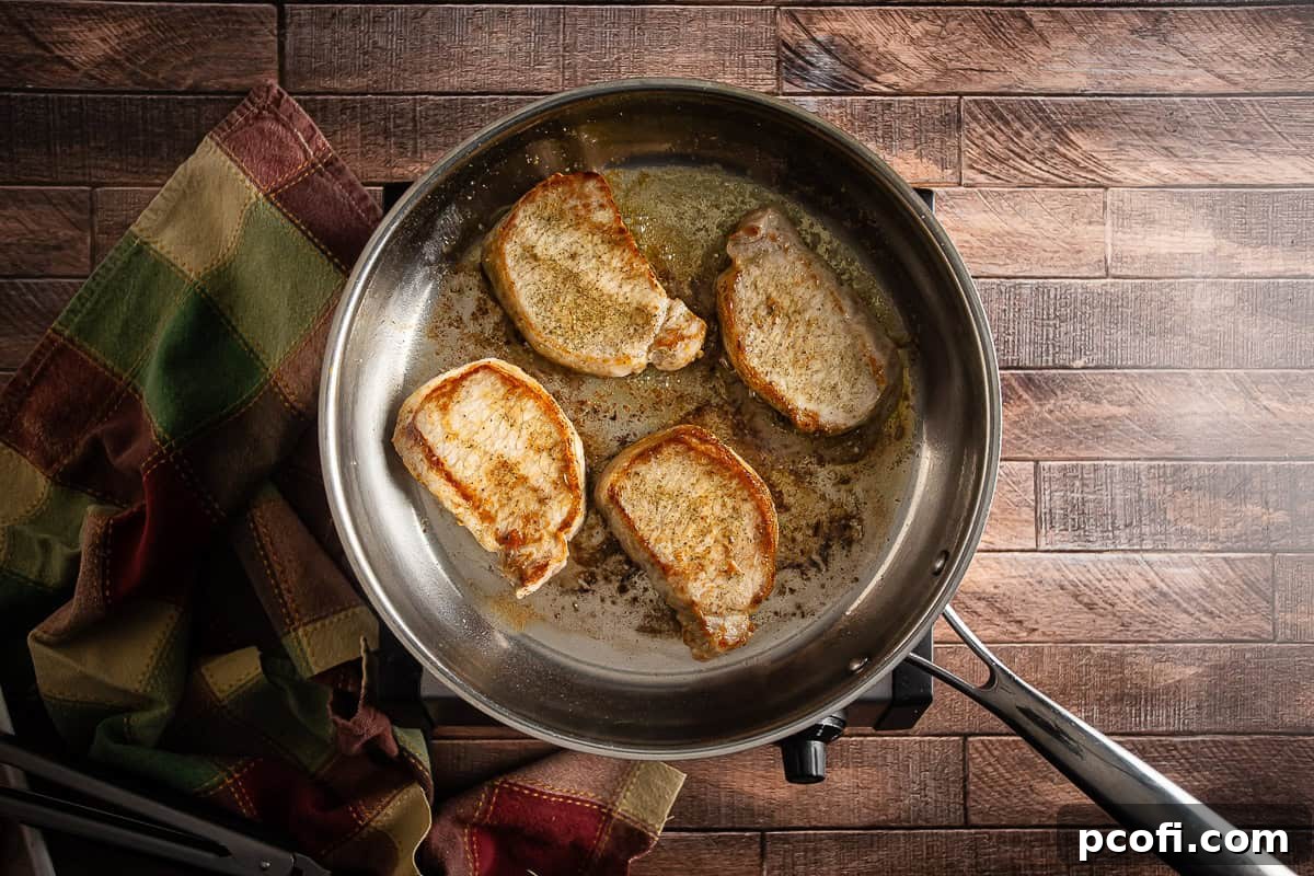 Pork chops in a skillet being browned on both sides for pork chops and apples.
