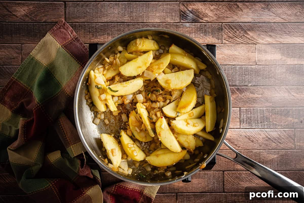 Sliced apples and sage added to sauteed onions in a skillet.