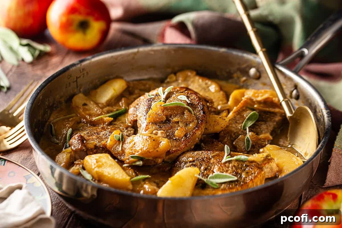 Pork chops and apples in a large skillet with a serving spoon and whole apples in the background.