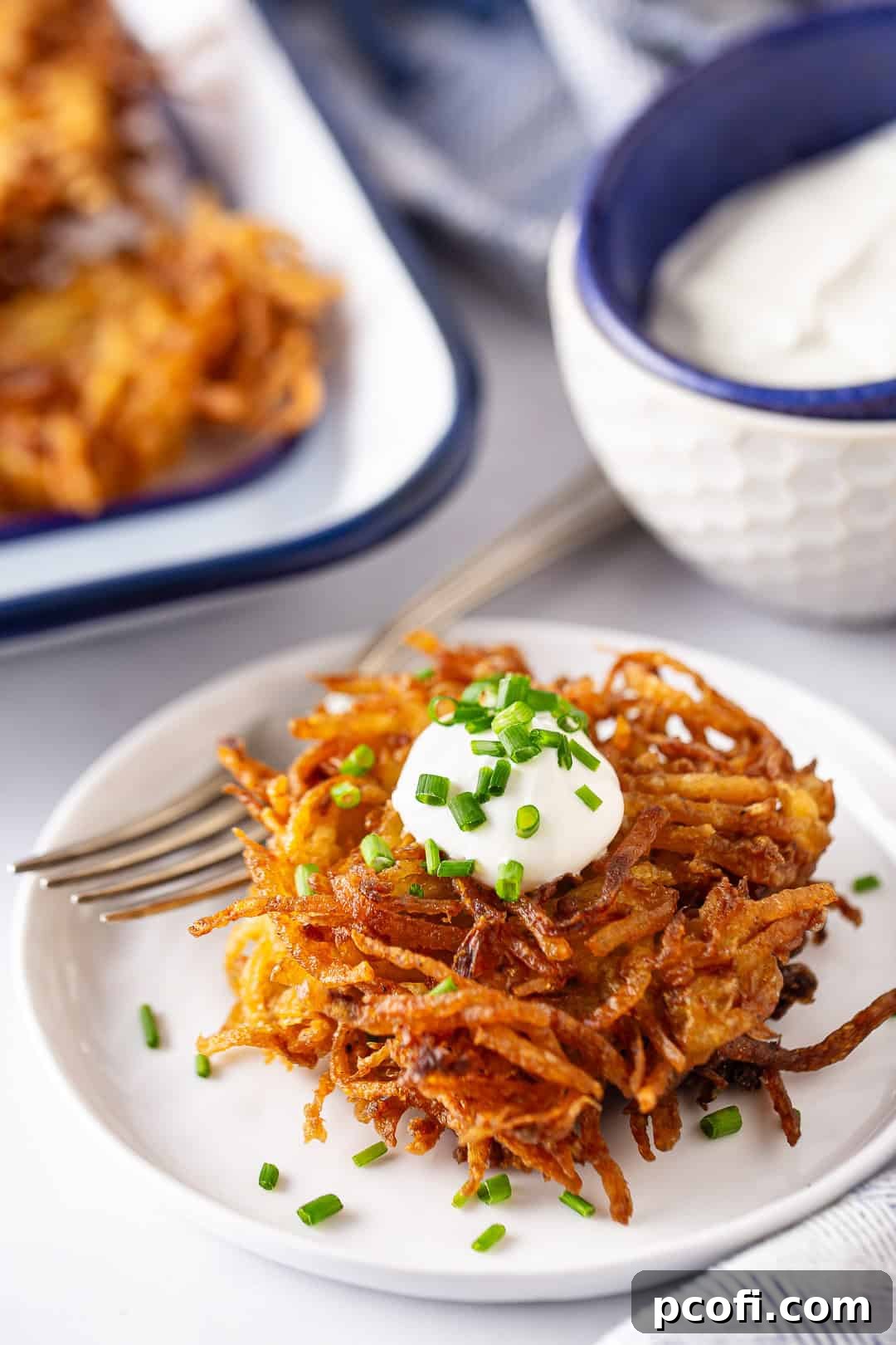 Potato pancakes in a stack with sour cream and chives on top, ready to be served.