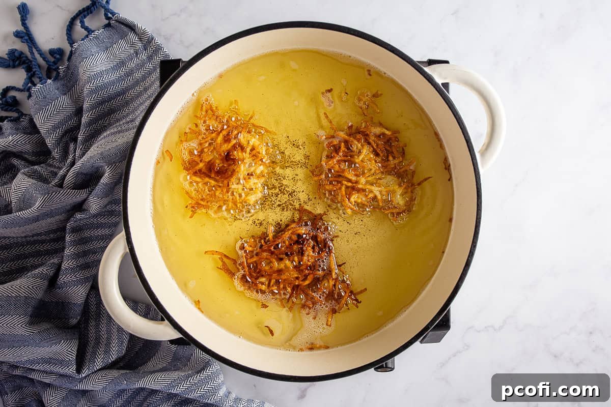 Several potato pancakes being fried to a golden brown in hot oil in a skillet.