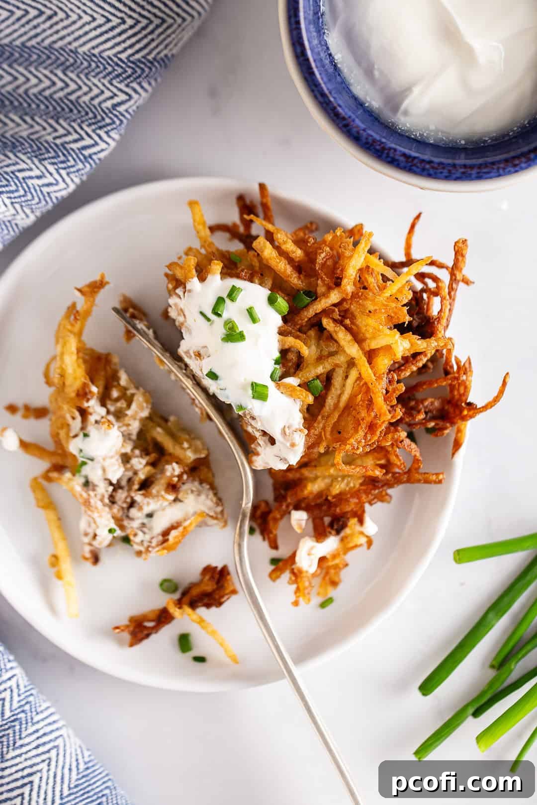 A crispy potato pancake with a bite taken out, topped with sour cream and chives.