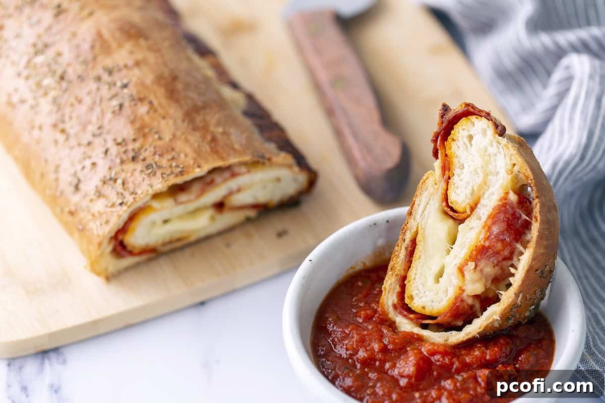 Slice of pepperoni bread dipped in a bowl of marinara sauce