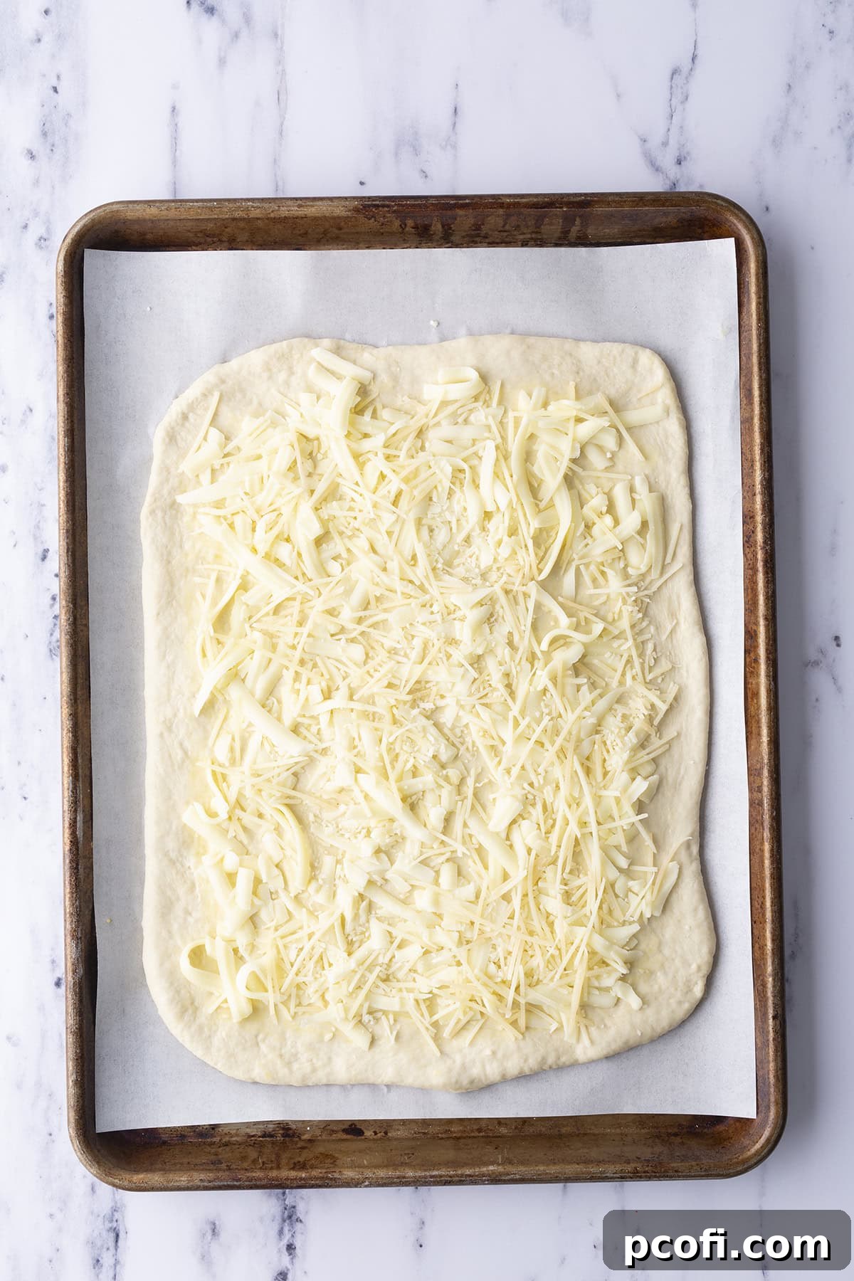 Shredded cheese spread over pizza dough