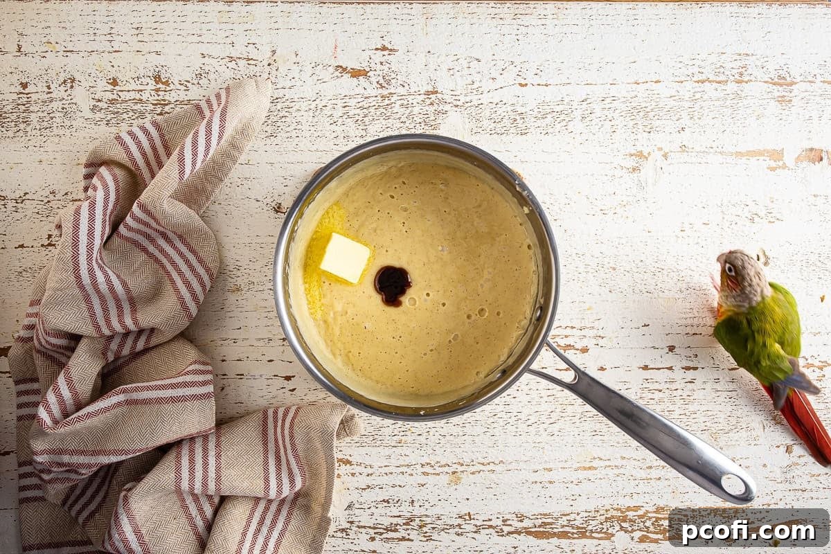 Cooked eggnog pie mixture in a medium saucepan, with butter and vanilla extract recently added and being stirred.