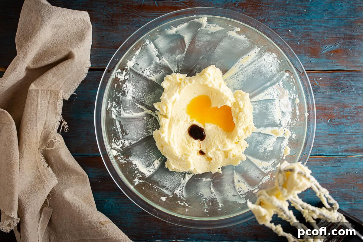 A glass mixing bowl containing creamed butter, powdered sugar, egg yolk, vanilla extract, and rum extract, all smoothly combined and ready for dry ingredients.