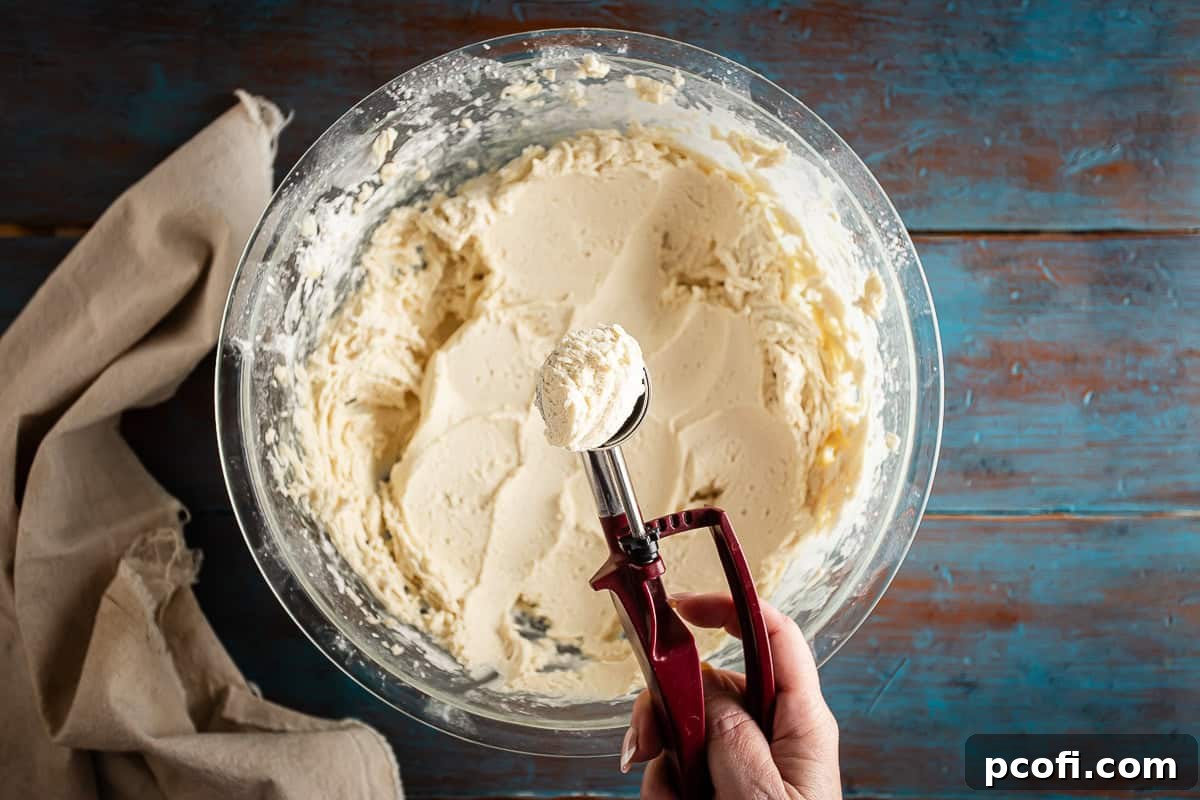 A perfectly portioned scoop of alfajores cookie dough held in a metal cookie scoop, ready for shaping.
