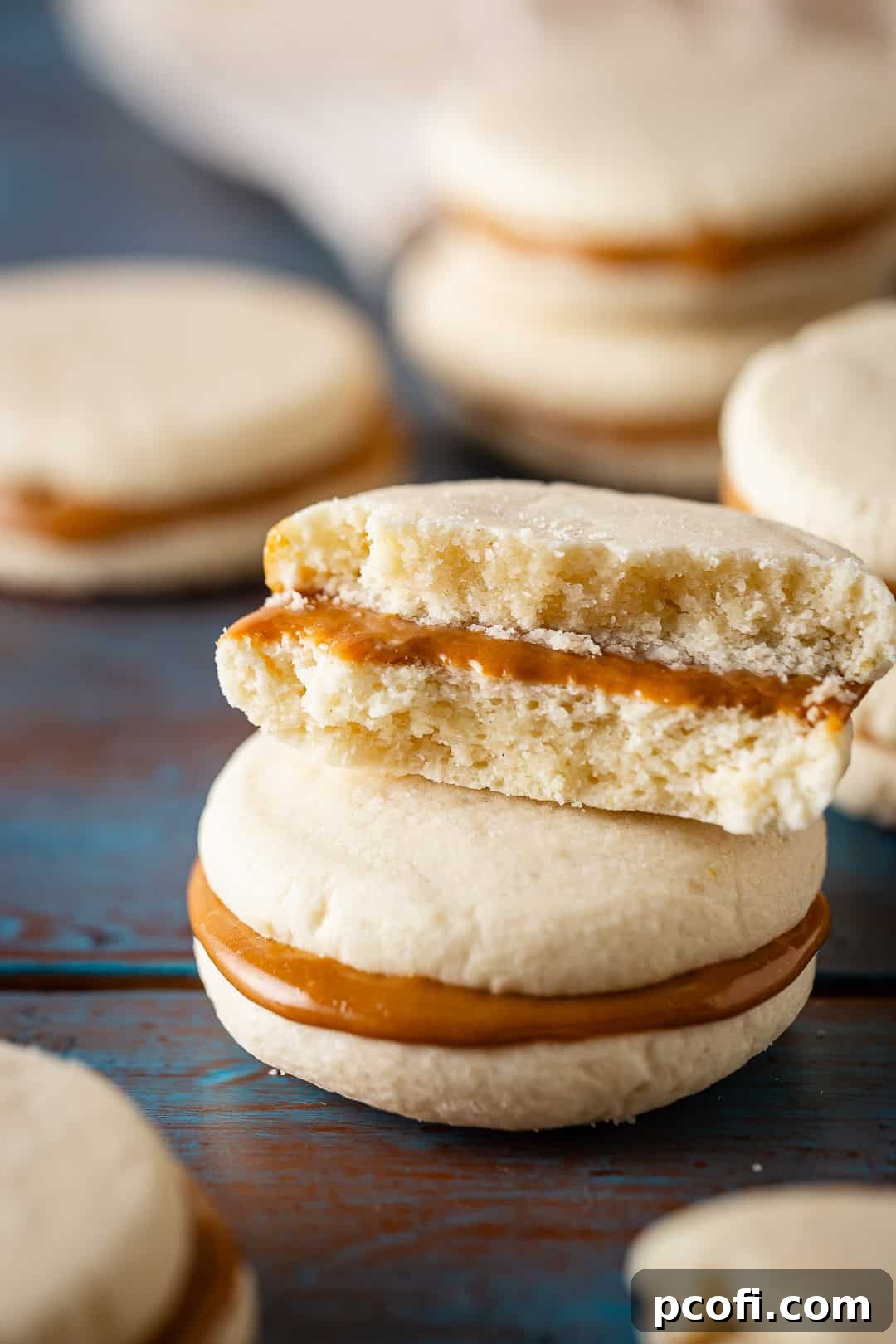 A stack of beautifully assembled Alfajores cookies, with one cookie broken in half to reveal the thick, luscious layer of dulce de leche filling between the tender cookie halves.