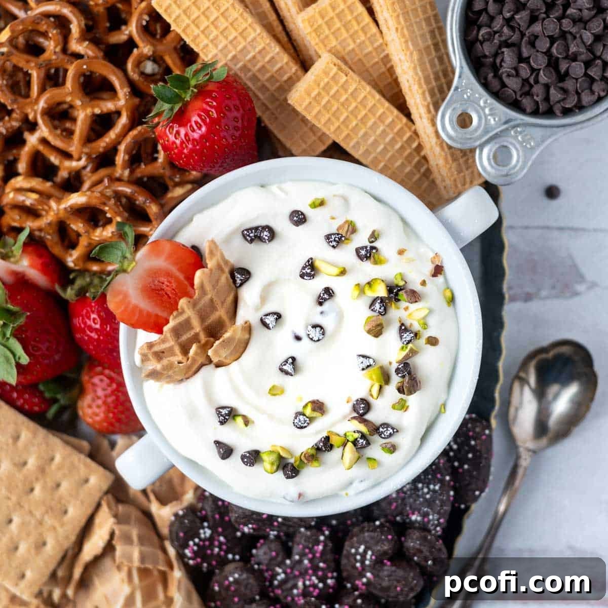 overhead look at cannoli dip with pistachios and chocolate chips on top. Surrounded by pretzels, strawberries and cookies.