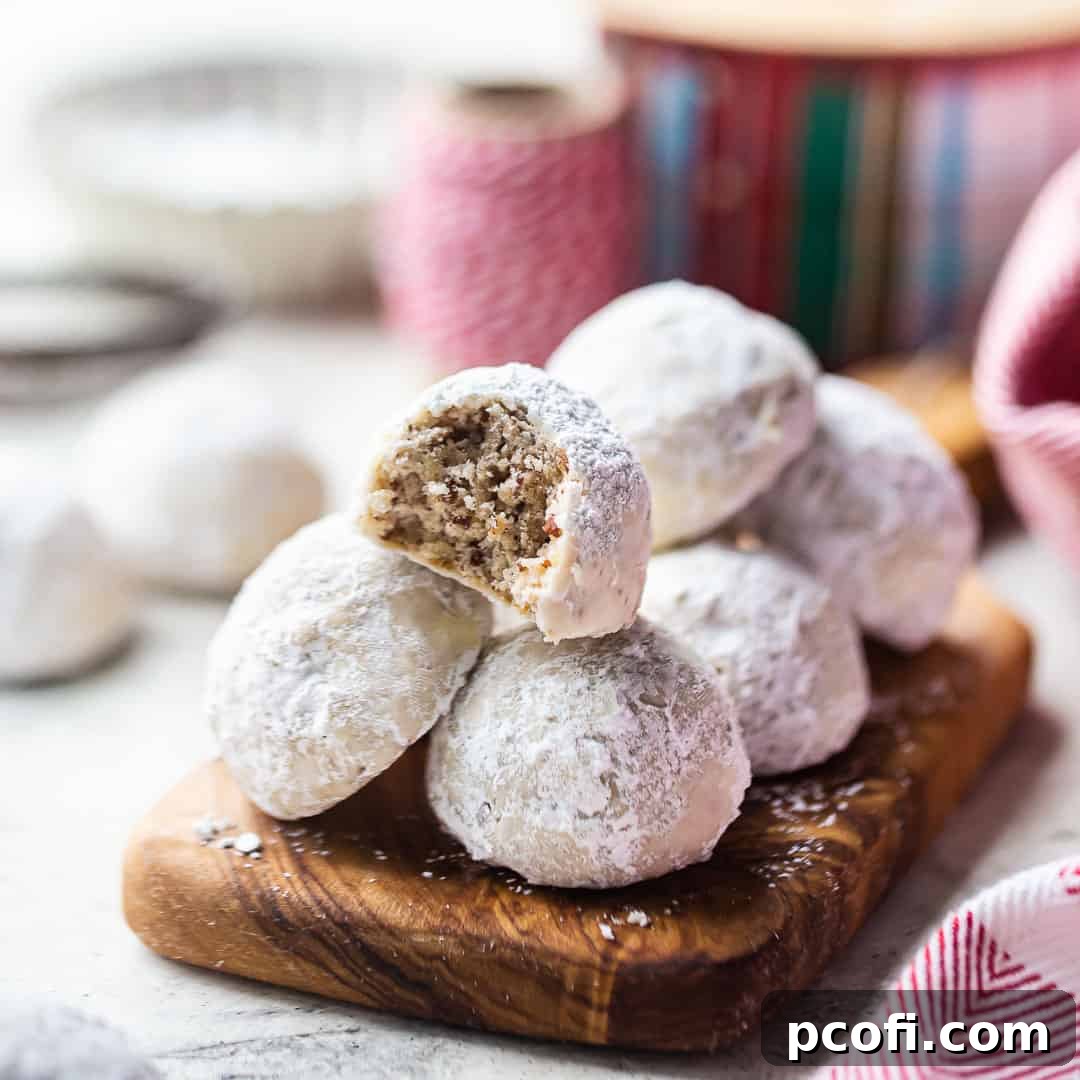 A beautiful stack of snowy Mexican Wedding Cookies on a wooden board with festive Christmas ribbon.