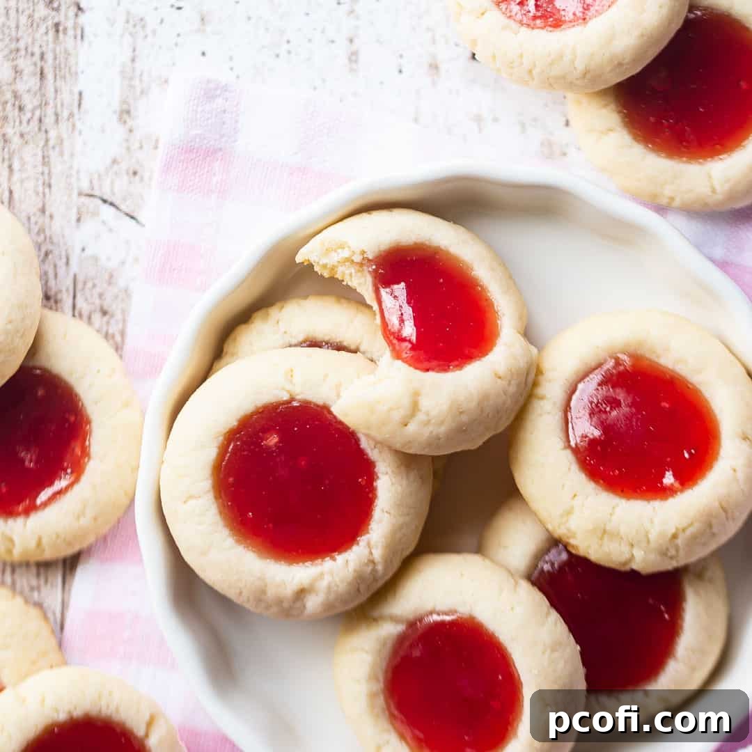 A collection of vibrant Jam Thumbprint Cookies in a white ceramic dish, with a charming pink gingham cloth.