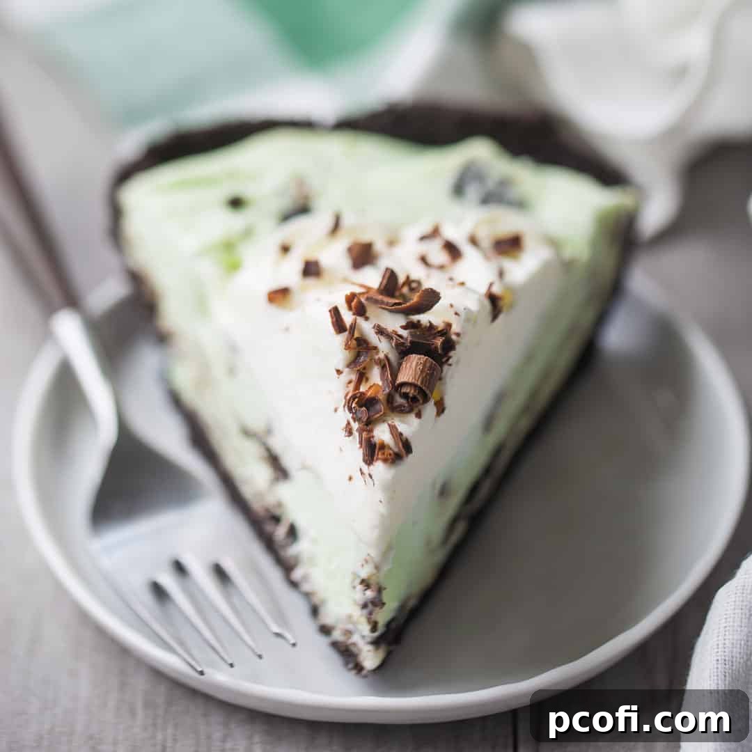 A slice of grasshopper pie with whipped cream and chocolate shavings, on a white plate with a green plaid napkin in the background.