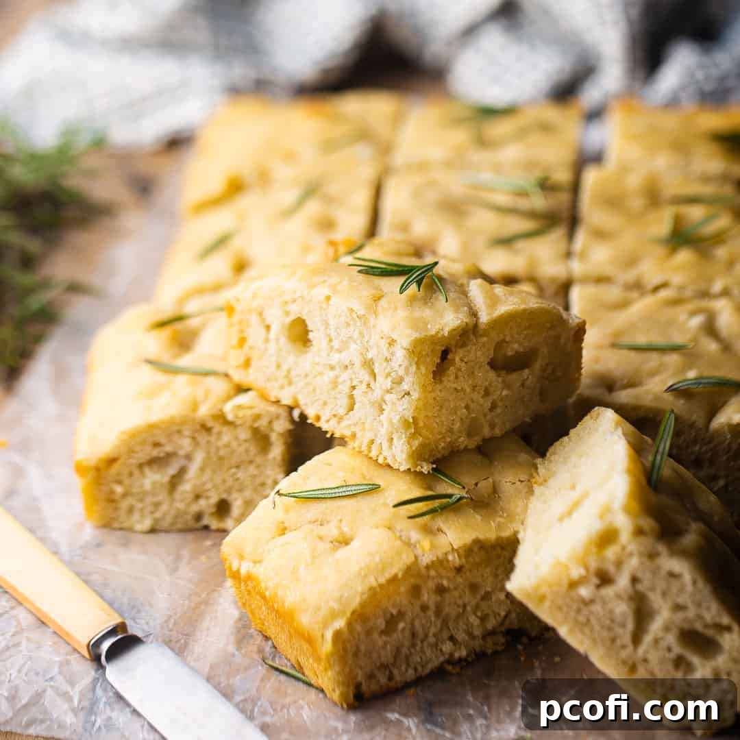 Squares of freshly baked focaccia bread stacked on a rustic wooden board, ready to be served.