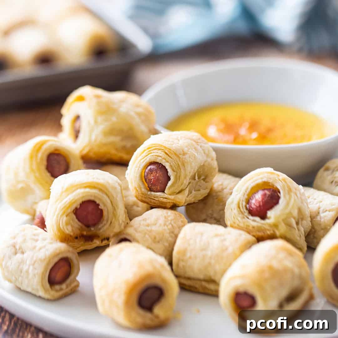A plate of golden-brown pigs in a blanket served with a bowl of honey mustard dip.