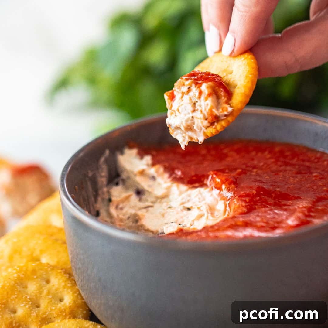 Scooping chilled crab dip from a bowl with a cracker, surrounded by lemon wedges and fresh dill.