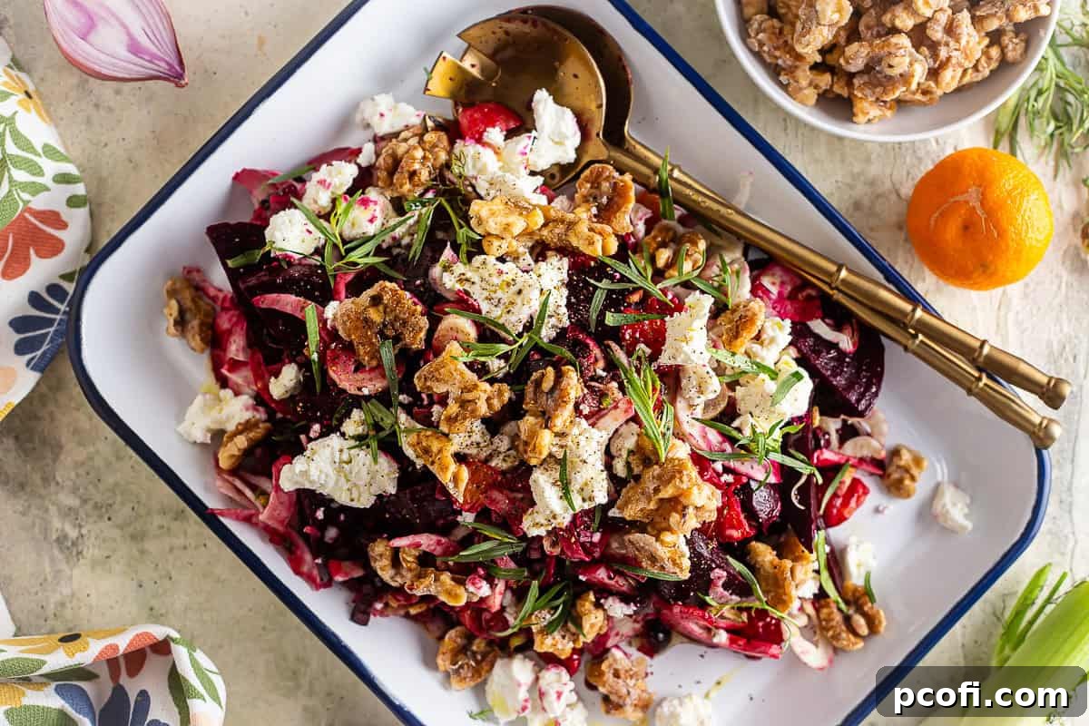 Finished beet salad on a serving platter with gold spoons, garnished with goat cheese and candied walnuts.
