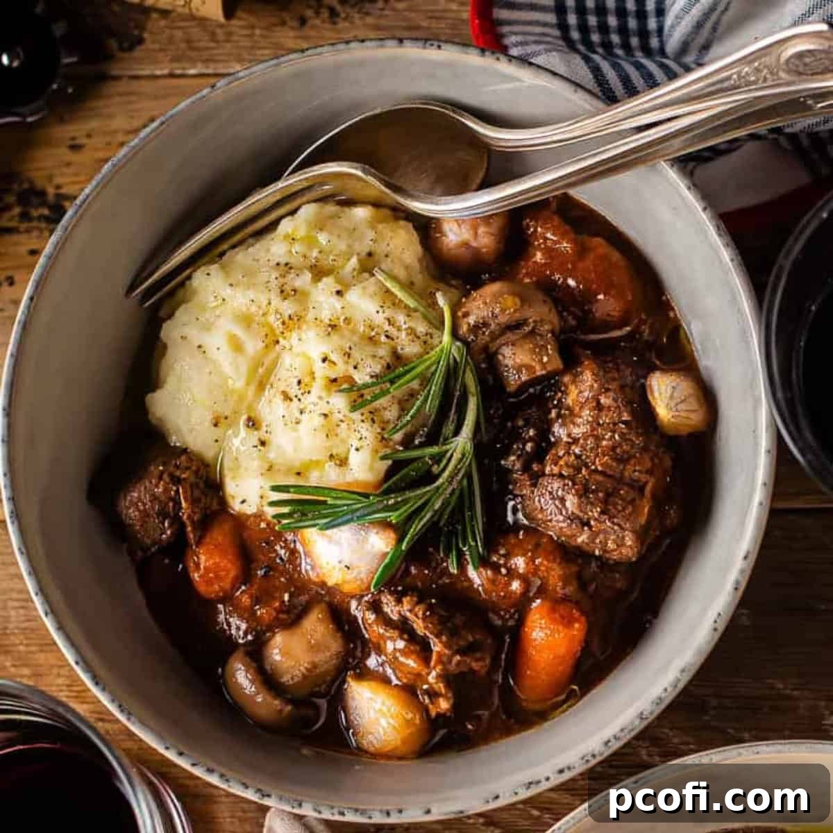 A hearty bowl of beef bourguignon with mashed potatoes, garnished with fresh rosemary.