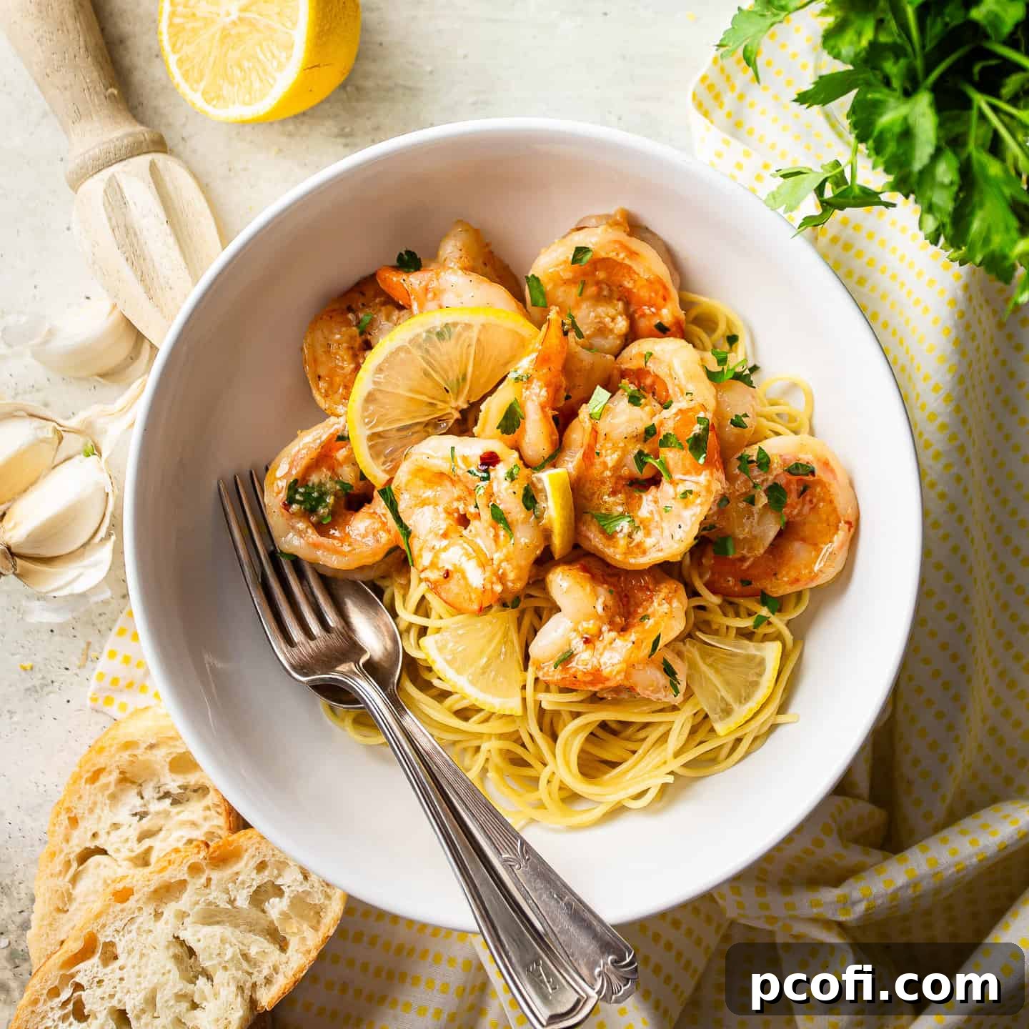 Garlicky, lemony shrimp scampi served over a bed of pasta in a white ceramic bowl.