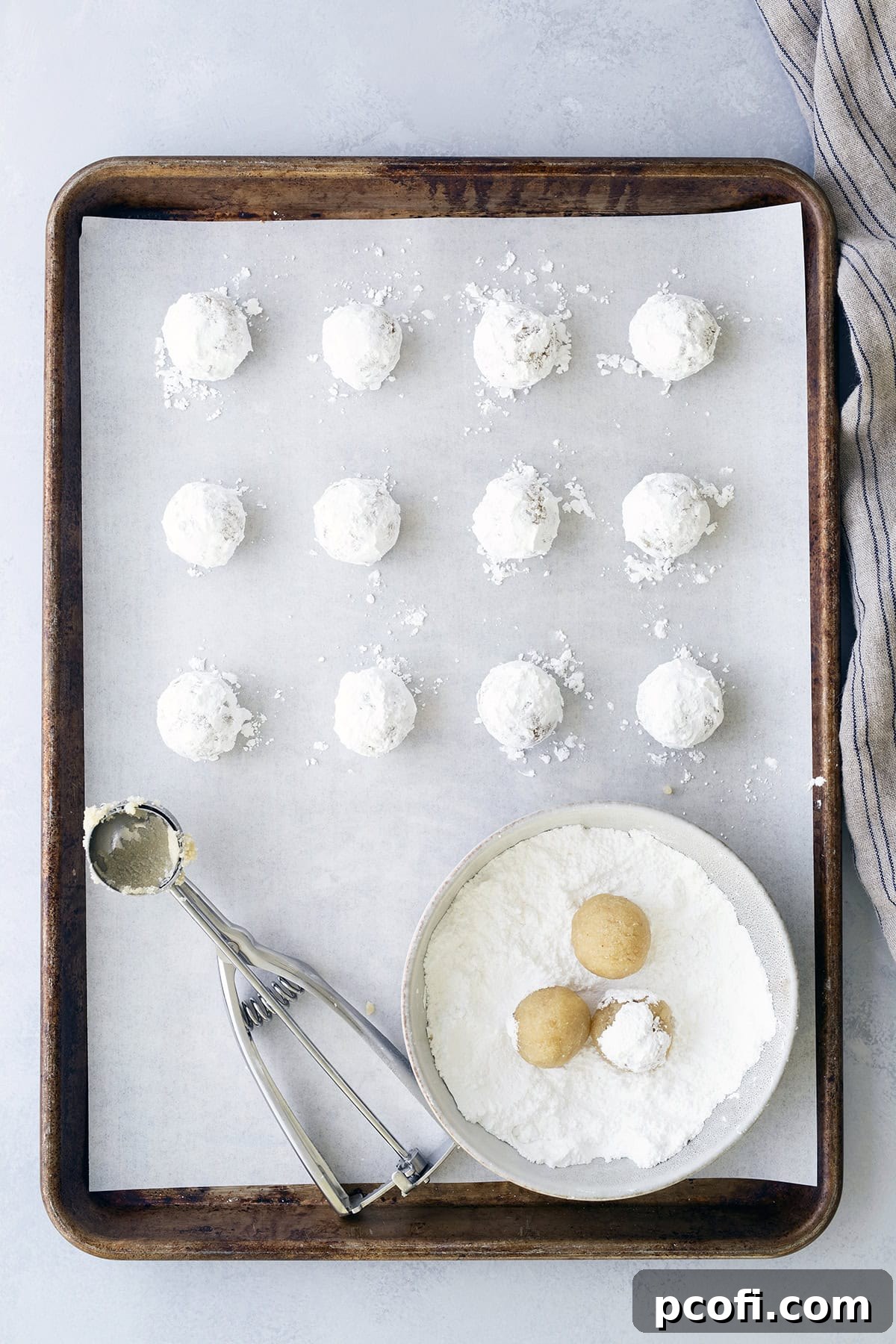 Unbaked cookies on baking pan after being rolled in powdered sugar.