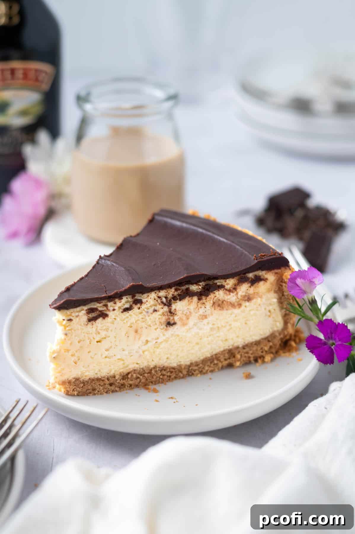 A delectable slice of Baileys cheesecake on a plate, with a glass of Irish cream and a bottle of Baileys in the softly blurred background.