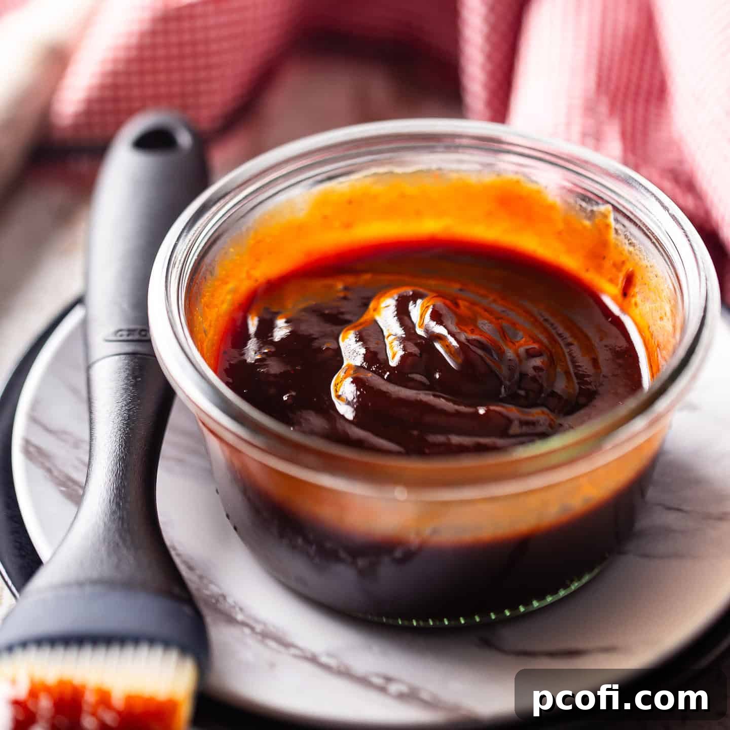 Glossy homemade barbecue sauce in a shallow glass dish with a basting brush, ready for grilling or dipping.