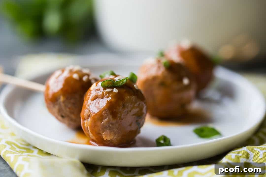 Sweet and sour meatballs on toothpicks, garnished with scallions and sesame seeds.