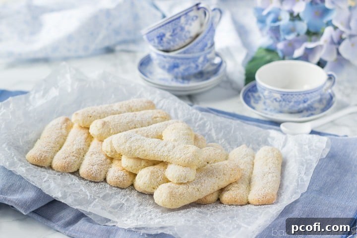 A beautifully arranged stack of homemade ladyfingers, some lightly dusted with powdered sugar, ready for serving or further dessert preparation.