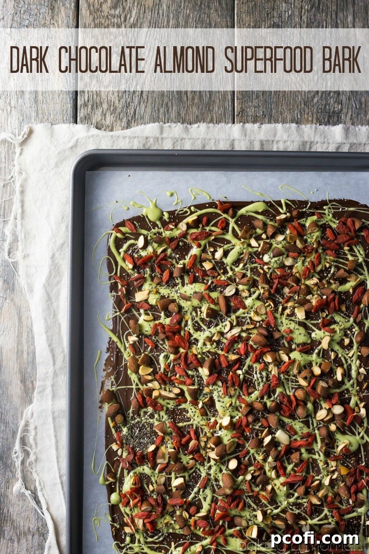 A close-up shot of Dark Chocolate Almond Superfood Bark, showcasing the vibrant green matcha drizzle, whole almonds, red goji berries, and tiny chia seeds on a rich dark chocolate base, emphasizing its health and visual appeal.