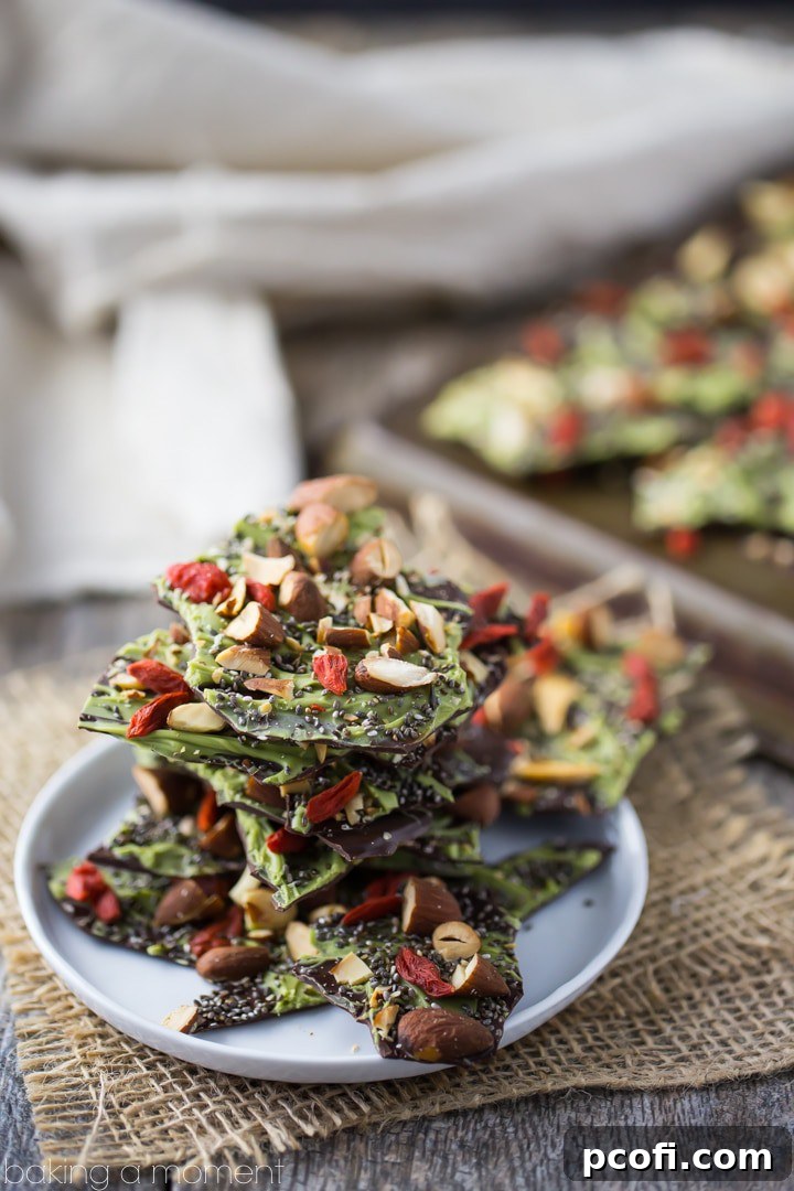 Delicious Dark Chocolate Almond Superfood Bark, garnished with a vibrant green matcha swirl, crunchy almonds, tangy goji berries, and nutritious chia seeds, ready to be broken into pieces.