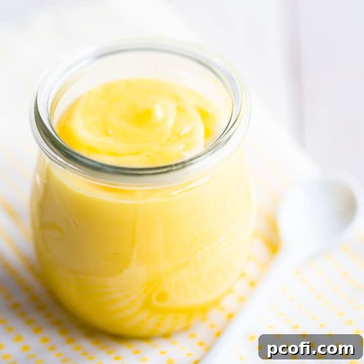 A small glass jar overflowing with vibrant yellow homemade lemon curd, set on a cheerful yellow and white checked cloth. Fresh lemons and a citrus reamer are nearby, highlighting the fresh ingredients.
