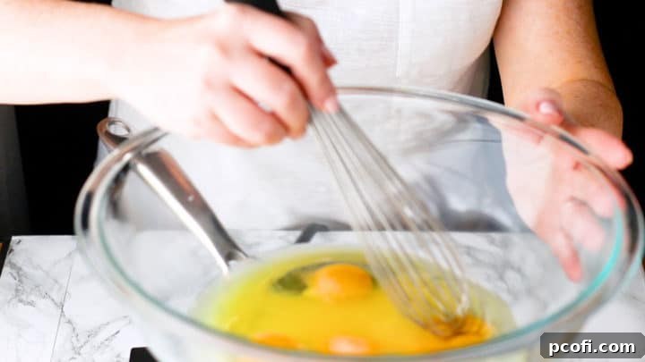Whisking eggs, granulated sugar, and fresh lemon juice together in a large mixing bowl, positioned over a pot of simmering water for gentle cooking.