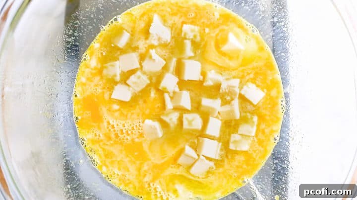 Adding small, cubed pieces of unsalted butter to the lemon curd mixture as it gently heats over a double boiler, preparing for melting and thickening.