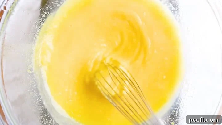 Actively whisking lemon curd over a double boiler until the mixture thickens visibly, and the whisk leaves clear tracks, indicating it's reached the perfect consistency.