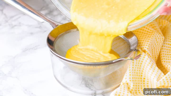 Straining freshly cooked homemade lemon curd through a fine-mesh sieve into a clean, heat-safe bowl to achieve an ultra-smooth and silky texture, removing any impurities.