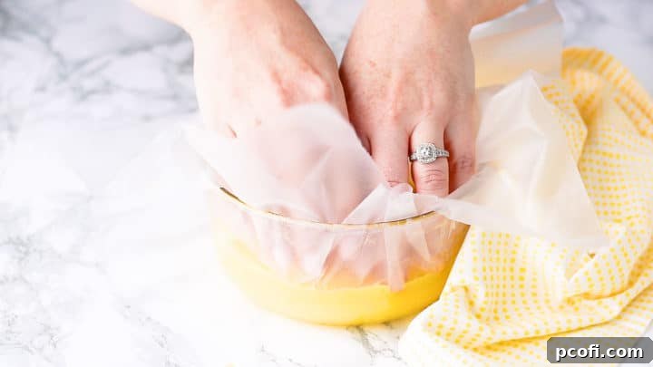 Pressing a sheet of plastic wrap directly onto the surface of freshly strained, warm lemon curd in a bowl. This prevents a skin from forming as the curd chills in the refrigerator.