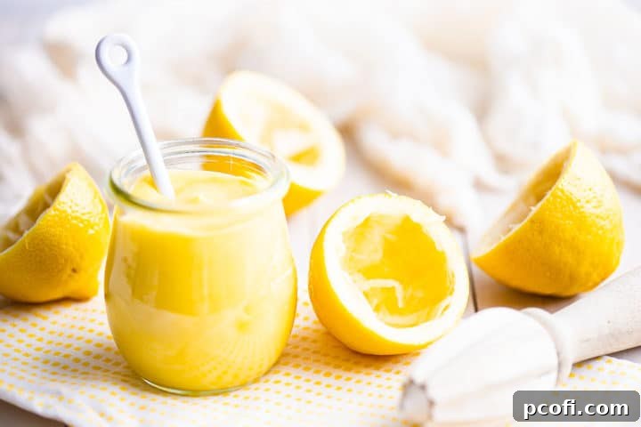 A beautifully presented small jar of homemade lemon curd, accompanied by a white ceramic spoon, suggesting its readiness to be enjoyed. The texture is smooth and inviting.