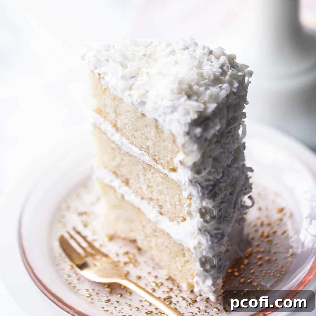 Tall slice of coconut cake on a pink plate with a gold fork, showcasing its luscious layers and fluffy frosting.